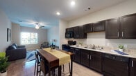 This single-story unit at 4702 Ambassador Way in Balch Springs, Texas, offers a well-organized layout with a cohesive modern design throughout. The open-concept kitchen and living area form the heart of the space, where dark espresso-toned cabinetry with sleek hardware contrasts against light granite-style countertops and wood-look flooring. Black appliances, including a full-size refrigerator, gas range, and microwave, are neatly integrated into the cabinetry. Recessed lighting illuminates the kitchen, while a ceiling fan serves the adjacent living area, which receives natural light through a window overlooking the exterior.

The bedroom is comfortably proportioned, featuring warm hardwood-style flooring, a ceiling fan, a window with exterior views, and direct access to a private bathroom. The bathroom is finished with tile flooring, a dark vanity with a white countertop, a large mirror, and a shower.

A second full bathroom mirrors this clean aesthetic, featuring tile flooring, a dark vanity, and a well-lit vanity mirror. A separate room accommodates a dedicated office or flex space, complete with hardwood-style flooring, a window, and ample wall space. Neutral gray tones and consistent finishes throughout give the unit a unified, understated character.