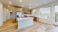 Located in Golden, Colorado, this thoughtfully designed single-floor home offers three bedrooms, three bathrooms, and a well-organized layout ideal for comfortable living. The modern kitchen serves as a centerpiece, featuring light wood cabinetry, white quartz countertops, a large center island, and a full suite of stainless steel appliances, including a refrigerator, range, and microwave. Recessed lighting and light wood-look flooring carry throughout the main living and kitchen areas, creating a bright, cohesive aesthetic. The living room benefits from natural light through large windows with views of the surrounding area. Each bedroom is carpeted for comfort, with neutral tones and ample closet space — including walk-in closets with wire shelving systems for organized storage. The primary bedroom offers a generous footprint with its own dedicated closet access. The bathrooms are finished in a clean, contemporary style, with warm wood vanities, white quartz countertops, large mirrors, and light wood-look tile flooring. One bathroom features a glass-enclosed walk-in shower, while another includes a soaking tub and shower combination. A dedicated laundry area and connecting hallway complete the functional floor plan of this well-appointed Golden home.