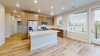 Located in Golden, Colorado, this well-designed single-floor home offers three bedrooms and three bathrooms with a cohesive modern aesthetic throughout. The open-concept kitchen is a standout feature, showcasing light wood cabinetry, stainless steel appliances including a French door refrigerator, electric range, and built-in microwave, complemented by a large central island with a crisp white quartz countertop. Light hardwood flooring and recessed lighting complete the kitchen's bright, contemporary feel. The bedrooms feature plush neutral carpeting and warm beige walls, creating a comfortable and restful atmosphere. The primary bedroom includes direct access to a private bathroom and a dedicated walk-in closet with wire shelving for organized storage. A second closet is also available elsewhere in the home. The bathrooms are finished with wood-toned vanities, white quartz countertops, and light hardwood-style flooring. One bathroom features a glass-enclosed walk-in shower with white tile surround, while another offers a full soaking tub. Hallways connect the rooms with smooth hardwood flooring, and panel-style interior doors add a clean, modern touch. Natural light filters in through multiple windows fitted with horizontal blinds, contributing to the home's bright and welcoming ambiance.