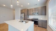 This single-story residence showcases a thoughtfully designed open-concept layout that seamlessly connects the living area and kitchen, creating a spacious and functional flow throughout. Light-toned hardwood-style flooring runs consistently across the main living spaces, complementing the clean, neutral color palette of the walls and trim.

The kitchen serves as a central hub, anchored by a sizeable white quartz-topped island with an undermount sink and pendant lighting above. Rich, medium-toned cabinetry extends to the ceiling, providing ample storage, while a white subway tile backsplash adds a contemporary touch. Stainless steel appliances, including a French door refrigerator with ice maker, an electric range, and a built-in microwave, complete the kitchen.

The living area benefits from natural light streaming through multiple windows fitted with horizontal blinds, and a ceiling fan adds both style and comfort. The bedrooms continue the hardwood-style flooring and include ceiling fans and windows with natural light.

The bathrooms are well-appointed; a primary bath features a dual-sink vanity with matching cabinetry, white quartz countertops, a walk-in shower with tile surround, and hardwood-style flooring. A secondary bath includes a soaking tub with tiled surround. Five-panel interior doors add a refined architectural detail throughout.