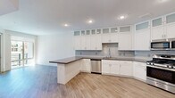Located at 4335 S Grand Canyon Dr in Las Vegas, Nevada, Unit 201 is a thoughtfully designed single-floor residence that makes excellent use of its intimate footprint. The open-concept layout seamlessly integrates the kitchen and living area, creating a bright and cohesive living space.

The kitchen is a standout feature, outfitted with crisp white shaker-style cabinetry that extends floor to ceiling, incorporating frosted glass upper panels for an elegant touch. A classic subway tile backsplash complements the dark countertops, while stainless steel appliances — including a refrigerator, range, microwave, and dishwasher — add a modern, polished finish. A peninsula counter provides additional prep space and doubles as a casual dining or gathering area.

Light-toned hardwood-style flooring runs throughout the entire unit, lending warmth and visual continuity. The living area is bathed in natural light through a large picture window that frames views of swaying palm trees and the surrounding landscape, evoking the vibrant Las Vegas setting. Recessed lighting throughout ensures the space remains well-lit at all hours.

Clean white walls and a neutral palette keep the interior feeling open and airy, offering a versatile canvas for personalization. The unit's efficient design and modern finishes make it a well-appointed residence in the heart of Las Vegas.
