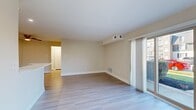 This single-floor residence offers a well-organized layout with distinct living, kitchen, bedroom, and bathroom areas. The main living space is bright and open, finished with light hardwood-style flooring that extends throughout the common areas. Large sliding glass doors allow generous natural light to fill the room while providing direct access to an outdoor patio area, offering views of the surrounding exterior grounds.

The kitchen is outfitted with medium-toned wood-finish cabinetry, white countertops, recessed lighting, and white appliances including a gas range, microwave, and refrigerator. The clean, functional design provides ample storage and workspace within a compact galley-style arrangement.

The bedroom is carpeted and features a window with blinds that admits natural light. A dedicated in-unit laundry area with a stacked washer and dryer is conveniently tucked behind closet-style doors within the unit.

The bathroom is finished with large-format tile on both the floor and the tub surround, complemented by chrome fixtures and a handheld showerhead. A vanity with a light countertop completes the space. Throughout the unit, neutral warm-beige walls and consistent finishes contribute to a cohesive and understated aesthetic.