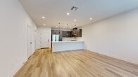 Located in Fontana, CA, this two-story home offers a clean, modern aesthetic across two well-defined levels. The ground floor is anchored by an open-concept living and kitchen area finished with light wood-tone flooring and crisp white walls that create a bright, airy atmosphere. The kitchen is a standout feature, equipped with gray shaker-style cabinetry extending to the ceiling, a white subway tile backsplash, a peninsula with a white countertop, stainless steel appliances, and stylish black pendant lighting. A staircase with a sleek black handrail connects to the upper level, which houses both bedrooms and two full bathrooms. The primary bedroom is a comfortable retreat with recessed lighting, a sliding glass door opening to a private balcony with outdoor views, and an additional window that invites natural light. A dedicated walk-in closet with built-in shelving and hanging rods offers generous storage. The bathrooms are finished with gray vanity cabinetry, white quartz countertops, large-format white wall tile, glass-enclosed showers, and matte black hardware, conveying a cohesive, contemporary style throughout.