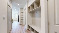 This single-story residence offers a thoughtfully designed layout across a comfortable footprint, combining modern aesthetics with practical functionality throughout. The open-concept kitchen and living area serves as the heart of the home, featuring light hardwood-style flooring, large windows with plantation shutters, and an abundance of natural light. The kitchen is equipped with stainless steel appliances, including a refrigerator, range, microwave, and a built-in wine cooler. Taupe cabinetry, a white subway tile backsplash, open display shelving, and a granite-topped island complete the space, with pendant lighting adding a polished finishing touch.

A dedicated built-in workstation with granite countertop, grey cabinetry, and overhead shelving provides a functional nook off the main living area. The hallway features an impressive built-in mudroom unit with cubbies, coat hooks, and a bench, alongside additional open shelving for storage.

Both bedrooms are carpeted and include ceiling fans, natural light from windows, and access to closets with hanging rods and shelving. The bathrooms are finished with granite-topped grey vanities, hardwood-style flooring, and tiled shower enclosures.