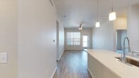 This well-appointed single-floor residence offers a thoughtfully designed open-concept layout that seamlessly connects the kitchen, dining, and living areas. The kitchen is a standout feature, showcasing crisp white shaker-style cabinetry with matte black hardware, a classic subway tile backsplash, light quartz countertops, and a full suite of stainless steel appliances including a range, microwave, and French door refrigerator. A central island provides additional prep space and casual seating. Pendant lighting and track lighting add warmth and functionality to the kitchen area. Light wood-look flooring flows throughout the main living spaces, complementing the neutral, warm-toned walls and creating a bright, cohesive aesthetic. The living area features a ceiling fan and is filled with natural light from windows overlooking a private exterior door. The bedrooms are finished with plush carpeting and neutral walls, offering a calm and restful atmosphere. Both bathrooms are well-equipped with white vanity cabinetry, quartz countertops, large mirrors, and tiled tub-shower combinations with light wood-look flooring. Additional practical features include a utility access panel and organized closet space. The overall design emphasizes clean lines, modern finishes, and a move-in-ready presentation.