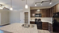 Located at 56 Bent Branch Loop in Clayton, NC, this single-floor residence offers a thoughtfully designed layout that balances functionality with comfortable living. The open-concept kitchen and living area serves as the heart of the home, where rich dark wood cabinetry pairs with granite countertops and a central island equipped with a stainless steel sink. Pendant lighting and track lighting illuminate the kitchen, which also features black appliances and a convenient walk-in pantry with wire shelving. Luxury vinyl plank flooring extends throughout the main living areas, providing a clean and cohesive look. Crown molding adds a refined architectural detail to the living space, which flows openly from the kitchen and benefits from natural light through a front-facing window. The bedrooms are carpeted for comfort and equipped with ceiling fans. One bedroom includes a walk-in closet with built-in shelving, offering ample storage. The bathroom features a tub-shower combination and wood-look vinyl flooring. A dedicated laundry room accommodates a full-size washer and dryer side by side, complete with overhead wire shelving. The overall ambiance is clean, neutral, and move-in ready.