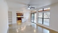 This single-floor residence offers a thoughtfully designed layout encompassing three bedrooms, two bathrooms, and a seamlessly connected living, dining, and kitchen area. Polished concrete floors run throughout the main living spaces, reflecting natural light and lending a clean, contemporary aesthetic to the interior.

The open-concept living and dining area is anchored by a ceiling fan and large sliding glass doors that provide direct access to an enclosed outdoor space, allowing abundant natural light and views of surrounding greenery to pour in. A pendant light fixture highlights the dining area, which also benefits from an oversized window framing tree-lined outdoor views.

The kitchen is well-equipped with rich, dark-stained wood cabinetry, granite countertops, stainless steel appliances including a gas range, microwave, and refrigerator, recessed lighting, and a central island with seating. A built-in wine rack adds a distinctive touch.

The bedrooms feature neutral walls, concrete or carpeted floors, and windows providing natural light. The primary bathroom includes a dual-sink vanity with dark wood cabinetry, a large mirror, and pendant lighting. Throughout, crown molding and white trim provide a refined finishing detail.