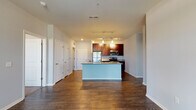 Located at 828 Niagara Preservation Cir in Kalamazoo, Michigan, this single-floor residence offers a thoughtfully designed open-concept layout. The kitchen serves as the focal point of the main living area, showcasing rich dark wood cabinetry, granite countertops, and a full suite of stainless steel appliances including a refrigerator, electric range, and over-the-range microwave. A large center island with a granite surface and integrated sink provides additional prep space and separates the kitchen from the living area. Track lighting and pendant lights illuminate the space, complementing the warm, dark hardwood-style flooring that runs throughout the main living areas. The open floor plan creates a generous, connected feel between the kitchen and living spaces, with a hallway leading to multiple rooms. The bedrooms feature plush carpeting and large windows fitted with horizontal blinds, allowing for ample natural light and exterior views of the surrounding greenery. Each bathroom is finished with granite-topped dark vanities, wood-style flooring, and a soaking tub with a shower combination. Clean white walls and neutral tones throughout create a cohesive, modern aesthetic suited for comfortable everyday living.