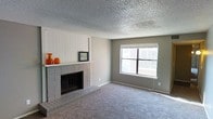 This single-floor residence offers a welcoming and functional layout centered around a standout living area. The focal point of the room is a classic brick fireplace framed by a crisp white vertical shiplap accent wall, complete with a mantel — an ideal spot for decorative accents. The fireplace adds both character and warmth to the space, lending it a cozy, timeless feel. Plush wall-to-wall carpeting in a neutral gray tone runs throughout the living area, providing comfort underfoot and a versatile backdrop for a variety of furnishing styles. A large, bright window on the adjacent wall allows generous amounts of natural light to flow in, enhancing the open and airy atmosphere of the room. The walls are finished in a soft, neutral gray, complementing the overall palette and contributing to a calm, understated aesthetic. The textured popcorn ceiling adds a layer of visual depth overhead. The overall ambiance is clean, comfortable, and move-in ready, making it a solid and practical living space with classic architectural details that offer both style and function.