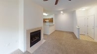 This single-story space is designed with a functional, open layout that connects the main living areas seamlessly. The living room serves as the central gathering space, featuring a tile-surround fireplace with a classic black insert as a focal point, neutral carpet flooring, and a ceiling fan overhead. An open-concept kitchen is directly accessible from the living area, separated by a peninsula breakfast bar with a clean white countertop that provides additional prep and seating space. The kitchen is equipped with medium-toned wood cabinetry, a white electric range, and a full-size refrigerator, with a built-in overhead light ensuring excellent visibility.

The bedrooms are generously proportioned, each finished with plush neutral carpet and ceiling fans. Natural light filters in through blinded windows that offer views of surrounding greenery. One bedroom includes a closet with built-in shelving, while another features a dedicated en-suite bathroom entry. The bathrooms are finished in white throughout, with tile flooring, a wide vanity with solid-surface countertops, a full mirror, and a tub-shower combination. The overall palette of crisp white walls and warm neutral carpeting creates a clean, move-in-ready ambiance.