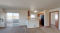 Located at 16102 East Broadway Avenue in Spokane Valley, Washington, this single-floor unit offers a well-organized and functional layout designed for comfortable everyday living. The open-concept living and dining area is finished with plush carpeting and features a sliding glass door that leads to a private balcony, filling the space with natural light and providing pleasant outdoor views of the surrounding neighborhood. The kitchen is thoughtfully designed with rich warm-toned wood cabinetry, light countertops, a double-basin sink beneath a window, and black appliances including a refrigerator, range, and dishwasher. A peninsula-style island divides the kitchen from the living area, creating an efficient and social flow between the two spaces. The bedrooms are carpeted, well-lit by windows, and offer clean, neutral walls that provide a versatile canvas for personalization. Two bathrooms serve the unit: one featuring hardwood-style flooring, a vanity with wood cabinetry, and a small privacy window, and a second with a full tub-and-shower combination and a large vanity mirror. Throughout the unit, wood-style flooring transitions seamlessly into carpeted areas, adding warmth and visual continuity to the overall design.
