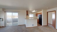 Located at 16102 East Broadway Avenue in Spokane Valley, Washington, this single-floor unit offers a well-organized and functional layout designed for comfortable everyday living. The open-concept living and dining area is finished with plush carpeting and features a sliding glass door that leads to a private balcony, filling the space with natural light and providing pleasant outdoor views of the surrounding neighborhood. The kitchen is thoughtfully designed with rich warm-toned wood cabinetry, light countertops, a double-basin sink beneath a window, and black appliances including a refrigerator, range, and dishwasher. A peninsula-style island divides the kitchen from the living area, creating an efficient and social flow between the two spaces. The bedrooms are carpeted, well-lit by windows, and offer clean, neutral walls that provide a versatile canvas for personalization. Two bathrooms serve the unit: one featuring hardwood-style flooring, a vanity with wood cabinetry, and a small privacy window, and a second with a full tub-and-shower combination and a large vanity mirror. Throughout the unit, wood-style flooring transitions seamlessly into carpeted areas, adding warmth and visual continuity to the overall design.