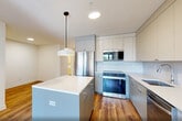 Located at 873 Communipaw Avenue in Jersey City, NJ, this well-appointed one-bedroom, one-bathroom residence offers a thoughtfully designed layout across a single floor. Warm hardwood-style flooring runs throughout the unit, complementing the clean, white walls that create a bright and modern aesthetic.

The open-concept living, dining, and kitchen area serves as the heart of the home. The kitchen is outfitted with floor-to-ceiling cabinetry in a soft grey-white palette, quartz countertops, a subway tile backsplash, stainless steel appliances including a gas range and dishwasher, and a central island with pendant lighting — ideal for both cooking and casual dining.

The bedroom is a comfortable, well-lit retreat featuring a large black-framed window that frames views of the surrounding Jersey City neighborhood and allows generous natural light. A wall-mounted split-unit air conditioner ensures climate control year-round. Two closets provide ample storage throughout the unit.

Two additional den spaces offer flexible use as a home office, guest room, or hobby area. The bathroom features a modern floating vanity with a vessel sink, vertical tile backsplash, and a mirrored medicine cabinet. In-unit laundry adds everyday convenience. The overall ambiance is clean, contemporary, and move-in ready.