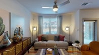 This single-story residence offers a thoughtfully designed layout with distinct living spaces that blend functionality and style. The open-concept kitchen serves as a central hub, featuring rich medium-toned wood cabinetry, a subway tile backsplash, black appliances, and a generous granite-topped island with seating. A pendant light fixture provides focused task lighting, while recessed ceiling lights illuminate the full kitchen area.

The living room is warm and inviting, centered around a large sofa accented with colorful throw pillows and anchored by a patterned area rug. A ceiling fan with integrated lighting provides air circulation, while multiple windows dressed with geometric-patterned curtains and horizontal blinds allow natural light to filter in. A glass-panel door provides direct access to an outdoor area with views of the surrounding community.

The bedroom is designed with comfort in mind, featuring plush carpeting, a bold upholstered headboard, sunburst mirrors, and natural wood wall art that adds organic texture. A window dressed with gold drapes introduces natural light and outdoor views.

The bathroom features rich wood cabinetry with granite countertops, a wide vanity mirror with bar lighting above, and durable wood-look flooring, completing this well-appointed residence.