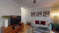 This thoughtfully designed two-bedroom, two-bathroom residence offers a comfortable and functional single-story layout. The living room is a welcoming central space, featuring warm hardwood-style flooring, crown molding, and a ceiling fan overhead. A large sliding glass door flanked by floor-length curtains fills the room with natural light, while built-in vertical blinds provide privacy when needed.

Adjacent to the living room, the dining area showcases rich hardwood flooring, a pendant light fixture, crown molding, and a built-in shelving nook — an ideal spot for décor or storage. A window overlooking greenery adds a pleasant outdoor connection.

The kitchen is well-equipped with white cabinetry, dark countertops, hardwood-style flooring, and full appliances including a refrigerator, electric range, and dishwasher, offering ample prep and storage space.

Both bedrooms are carpeted and generously sized, each offering closet access and a calm, neutral palette. The two bathrooms are distinct — one features a sliding-door shower enclosure with hardwood-style flooring, while the second offers a full tub-shower combination with tiled surround, providing versatile bathing options for residents.