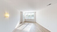 This well-designed single-floor unit offers a clean, contemporary aesthetic defined by a crisp white and neutral color palette, light wood-tone flooring, and an abundance of natural light. The open-concept living area is generously proportioned, featuring large windows fitted with horizontal blinds that allow natural light to stream in and cast warm patterns across the floor. A wall sconce adds a welcoming touch to the living space.

The kitchen is a functional and stylish centerpiece of the unit, anchored by a white kitchen island with a built-in sink and light stone countertops. Warm wood-toned cabinetry lines the kitchen walls, complemented by stainless steel appliances including a refrigerator, electric range, and microwave. Pendant lighting hangs above the island, adding both illumination and a decorative element. The kitchen flows seamlessly into the living and dining areas, making the layout highly practical for everyday living.

The bathroom is finished with a clean, modern sensibility, featuring a white vanity with an integrated sink, a large mirror with overhead lighting, and gold-toned hardware accents including towel bars. Hexagonal tile flooring adds subtle texture to the space.

Overall, the unit presents a bright, move-in-ready environment with consistent modern finishes and a thoughtful, open layout.