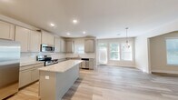 Located in Lawrenceville, GA, this well-appointed two-story home offers five bedrooms and four bathrooms across two thoughtfully designed floors. The main level features an open-concept layout connecting the kitchen, dining room, and living area, all finished with light wood-look flooring that lends a clean, modern aesthetic. The kitchen is a standout, boasting gray shaker-style cabinetry, granite countertops, a center island, stainless steel appliances, and recessed lighting. A glass-paned back door and large windows in the dining area flood the space with natural light and provide views of the surrounding greenery. The upper level houses the generous primary bedroom, distinguished by a tray ceiling, ceiling fan, plush carpeting, and a walk-in closet fitted with wire shelving. Additional bedrooms are well-sized and share access to well-appointed bathrooms, each with granite vanity tops and light wood-look flooring. A dedicated laundry room with utility connections adds everyday convenience. Hallways are bright and airy, featuring tall ceilings and white panel doors that maintain a cohesive, fresh look throughout. The home is designed with functionality and comfort in mind, making it an excellent fit for a variety of living needs.