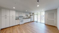 This single-floor unit is designed with a clean, contemporary aesthetic throughout. The open-concept kitchen and living area serves as the heart of the space, featuring light wood-style flooring, recessed lighting, and white cabinetry extending floor to ceiling for generous storage capacity. The kitchen is equipped with white appliances, including an electric range, built-in microwave, dishwasher, and refrigerator, complemented by gray laminate countertops and a stainless steel sink. Large floor-to-ceiling windows with vertical blinds allow abundant natural light to fill the space while offering views of the surrounding greenery outdoors.

The bedrooms are carpeted and offer a quiet, comfortable atmosphere, each featuring a ceiling fan with light fixture and a closet with built-in shelving for organized storage. One bedroom features a large window with vertical blinds, further enhancing natural light throughout.

The bathroom is finished with marble-style tile flooring and includes a full-size soaking tub with an overhead shower, coordinating brushed gold fixtures, and a white vanity. The overall design palette of whites, grays, and neutral tones creates a cohesive and bright living environment throughout the unit.