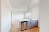 Located at 1 E Main Street, Unit 608 in Bound Brook, NJ, this thoughtfully designed one-bedroom, one-bathroom residence offers a clean, contemporary aesthetic with efficient use of space throughout. Light hardwood flooring flows seamlessly across the open-concept living, dining, and kitchen area, creating a cohesive and airy atmosphere. The kitchen serves as the focal point of the main living space, featuring sleek gray cabinetry, a striking waterfall-edge quartz island with an undermount sink, stainless steel appliances including a refrigerator, range, microwave, and dishwasher, and a decorative hex tile backsplash. A pendant light above the island adds a modern touch, while a window allows natural light to brighten the space. In-unit stacked washer and dryer are conveniently tucked nearby. The bedroom offers a calm, neutral palette with soft gray walls, a window with outdoor views, a dedicated closet, and hardwood flooring. The bathroom is finished with large-format tile flooring, a vanity with under-cabinet storage, a framed mirror, and a glass-enclosed walk-in shower with full tile surround. White Shaker-style and louvered doors, black hardware accents, and crisp white trim complete the polished, modern look of this well-appointed home.