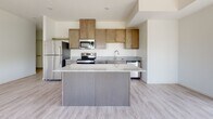 This single-floor unit presents a thoughtfully designed open-concept layout, where the kitchen and living area flow seamlessly together. The kitchen is equipped with medium-toned wood cabinetry, granite countertops, stainless steel appliances including a range, microwave, dishwasher, and refrigerator, and a central island that provides additional workspace and storage. Light wood-look plank flooring extends throughout the main living area, enhancing the bright, airy atmosphere created by multiple windows that frame outdoor views of greenery and a nearby water feature.

The spacious living area benefits from generous natural light streaming through a bank of windows, giving the room an open and inviting feel. Bedrooms are finished with plush carpet and feature dedicated closets with built-in shelving for organized storage. One bedroom offers a scenic outdoor view.

The bathrooms are well-appointed, with the primary bath featuring dark wood cabinetry, a granite-topped vanity, a tall linen tower, tile flooring, and a large mirror with modern lighting. The secondary bathroom includes a tub-shower combination, granite vanity, dark wood cabinetry, and tile flooring, maintaining a consistent, refined aesthetic throughout the unit.