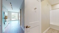 This well-designed single-floor unit offers a bright and modern living experience through a thoughtful open-concept layout. Light hardwood flooring flows consistently throughout the space, creating a cohesive and warm aesthetic. The entry hallway features a classic two-panel white door with brushed brass hardware and a sliding barn-style door, adding a contemporary touch to the transition into the main living area.

The open living and kitchen area is a standout feature of this unit. A floor-to-ceiling window wall floods the living space with abundant natural light while providing inviting outdoor views of surrounding greenery. The kitchen is well-appointed with crisp white shaker-style cabinetry, granite countertops, a stainless steel undermount sink, and a full suite of stainless steel appliances including a refrigerator, electric range, over-the-range microwave, and dishwasher. Track lighting above the kitchen adds functional illumination.

The bedroom is a generously sized, quiet retreat with its own large window that brings in natural light and garden views, complemented by neutral-toned walls and the same warm hardwood flooring.

The bathroom is finished with clean, modern tile work featuring a full-size soaking tub and shower combo with white subway-style wall tiles, chrome fixtures, a granite-topped vanity, and light floor tiles, all contributing to a polished, functional space.