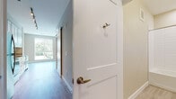 This well-designed single-floor unit offers a bright and modern living experience through a thoughtful open-concept layout. Light hardwood flooring flows consistently throughout the space, creating a cohesive and warm aesthetic. The entry hallway features a classic two-panel white door with brushed brass hardware and a sliding barn-style door, adding a contemporary touch to the transition into the main living area.

The open living and kitchen area is a standout feature of this unit. A floor-to-ceiling window wall floods the living space with abundant natural light while providing inviting outdoor views of surrounding greenery. The kitchen is well-appointed with crisp white shaker-style cabinetry, granite countertops, a stainless steel undermount sink, and a full suite of stainless steel appliances including a refrigerator, electric range, over-the-range microwave, and dishwasher. Track lighting above the kitchen adds functional illumination.

The bedroom is a generously sized, quiet retreat with its own large window that brings in natural light and garden views, complemented by neutral-toned walls and the same warm hardwood flooring.

The bathroom is finished with clean, modern tile work featuring a full-size soaking tub and shower combo with white subway-style wall tiles, chrome fixtures, a granite-topped vanity, and light floor tiles, all contributing to a polished, functional space.