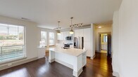 This single-floor residence offers a thoughtfully designed open-concept layout that combines style and functionality. The centerpiece of the home is the kitchen, which features crisp white cabinetry extending to the ceiling, stainless steel appliances including a French door refrigerator and electric range, a tile backsplash, and a large center island with a built-in sink and open shelving below. Pendant lights with brass accents and a track lighting system illuminate the space, complementing the rich dark hardwood floors that flow throughout the main living areas. A dedicated built-in hutch with shelving adds a charming storage element near the kitchen. The living area is generously sized, bathed in natural light through expansive windows with views of the surrounding area, and finished with a ceiling fan. Bedrooms are carpeted for comfort and feature windows and ceiling fans, while a walk-in closet with multiple shelving rods offers ample storage. Both bathrooms are finished with light tile flooring, white cabinetry with chrome hardware, extended vanities with white countertops, large mirrors, and combination tub-shower units clad in neutral tile. The overall ambiance is clean, bright, and move-in ready, with a cohesive neutral palette throughout.