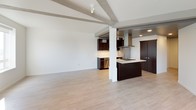 This studio offers a thoughtfully designed single-floor layout that maximizes its open-concept living space. The main living area makes an immediate impression with exposed ceiling beams that add architectural character, light hardwood flooring that runs throughout, and multiple windows that invite natural light from multiple angles, creating a bright and airy atmosphere.

The kitchen is a standout feature, designed with rich dark espresso cabinetry extending floor to ceiling for ample storage, complemented by a light stone-look countertop and a coordinating backsplash. A center island with an integrated cooktop provides additional workspace and casual dining potential. Stainless steel appliances, including a full-size refrigerator, dishwasher, and range, complete the modern aesthetic. Track lighting overhead ensures well-lit task areas throughout the kitchen.

The bathroom maintains the clean, contemporary design language found throughout the studio. It features light-toned tile flooring, a floating dark vanity topped with a marble-look stone countertop and undermount sink, a large mirror, and crisp white walls that give the space a polished, open feel. Recessed lighting provides clear, even illumination throughout.