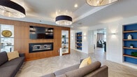 Located at 1407 South Michigan Avenue in Chicago's South Loop, this generously sized amenity floor spans a single level and offers a thoughtfully designed mix of entertainment, dining, and relaxation spaces. The interior is anchored by a striking living lounge with herringbone-patterned hardwood floors, a bold warm-wood accent wall housing a sleek fireplace and mounted TV, and statement drum pendant lighting that adds a modern, refined touch. Adjacent to the lounge is a full kitchen and café bar area, outfitted with warm wood cabinetry, stainless steel appliances, open display shelving set against vibrant blue recessed alcoves, and a white quartz island with rustic wood detailing — ideal for entertaining. A dedicated home theater features rows of plush leather reclining seats with built-in cup holders and floor-to-ceiling curtains for an immersive cinematic experience. The game room is flooded with natural light through expansive floor-to-ceiling windows overlooking the Chicago skyline, and is equipped with a pool table and ping pong table. A casual dining nook with upholstered banquette seating offers views of the landscaped outdoor terrace, which serves as a pool deck complete with lounge seating and greenery.
