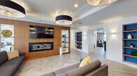 Located at 1407 South Michigan Avenue in Chicago's South Loop, this generously sized amenity floor spans a single level and offers a thoughtfully designed mix of entertainment, dining, and relaxation spaces. The interior is anchored by a striking living lounge with herringbone-patterned hardwood floors, a bold warm-wood accent wall housing a sleek fireplace and mounted TV, and statement drum pendant lighting that adds a modern, refined touch. Adjacent to the lounge is a full kitchen and café bar area, outfitted with warm wood cabinetry, stainless steel appliances, open display shelving set against vibrant blue recessed alcoves, and a white quartz island with rustic wood detailing — ideal for entertaining. A dedicated home theater features rows of plush leather reclining seats with built-in cup holders and floor-to-ceiling curtains for an immersive cinematic experience. The game room is flooded with natural light through expansive floor-to-ceiling windows overlooking the Chicago skyline, and is equipped with a pool table and ping pong table. A casual dining nook with upholstered banquette seating offers views of the landscaped outdoor terrace, which serves as a pool deck complete with lounge seating and greenery.