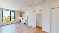 Located on the fifth floor at 282 Bremen St in Boston's East Boston neighborhood, Unit 512 is a thoughtfully designed studio that maximizes every inch of its compact footprint. The open-plan layout is anchored by light wood-tone flooring that runs throughout, complemented by crisp white walls and recessed lighting that create a clean, modern aesthetic.

The kitchen is a standout feature, outfitted with a full suite of stainless steel appliances including a range with oven, built-in microwave, dishwasher, and refrigerator. Cabinetry combines warm wood-tone upper cabinets with white shaker-style lower cabinets, topped with light countertops and a matte black sink fixture. A walk-in closet adjacent to the kitchen provides generous storage rarely found in similarly sized units.

The main living area is bright and airy, thanks to a large picture window framing treetop views of the surrounding Boston neighborhood, allowing abundant natural light to fill the space.

The bathroom is finished with contemporary details, including a wood-tone vanity with a gray quartz countertop, an undermount sink with a matte black faucet, a framed rectangular mirror, and stylish wall sconces. Blue hexagonal floor tiles add a distinctive design touch. The overall ambiance is modern, clean, and efficiently organized.