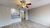 This single-floor unit offers a practical and efficiently organized layout, encompassing a living room, kitchen, bathroom, and hallway within a compact footprint. Light wood-style vinyl flooring runs consistently throughout the space, lending a clean, cohesive look that connects each area visually.

The living room serves as the central space of the unit, featuring neutral gray walls, a textured popcorn ceiling, and a ceiling fan with an integrated light fixture. A wall-mounted air conditioning unit and a window with blinds provide climate control and natural light. A closet accessible from the living area offers convenient built-in storage.

The kitchen is positioned adjacent to the living room in an open-plan arrangement, separated by a peninsula counter finished with a gray speckled laminate surface. White cabinetry provides ample storage above and below, complemented by a tiled backsplash, a double-basin sink, and a black electric range. A textured ceiling and flush-mount lighting complete the kitchen's functional design.

The bathroom features wood-style tile flooring, a vanity with a speckled countertop and under-sink cabinetry, a wall-mounted mirror with lighting, and a separate room housing the toilet and a full bathtub with a shower surround. The hallway connects the main living areas to the bathroom and includes a closet, maintaining an organized flow throughout the unit.