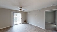 This single-floor residence offers a thoughtfully designed layout with a clean, neutral aesthetic throughout. The living area is open and airy, featuring light wood-style flooring, soft gray walls, a textured ceiling, and a ceiling fan with built-in lighting. A sliding glass door floods the room with natural light and provides direct access to an outdoor area, where glimpses of a pool and surrounding greenery can be seen.

The kitchen is well-equipped and modern, showcasing white shaker-style cabinetry with matte black hardware, granite-look countertops, a white subway tile backsplash, and stainless steel appliances including a refrigerator, dishwasher, and range. A peninsula counter extends into the adjacent dining or living space, enhancing the open feel. Light wood-style flooring continues here, complementing the bright, overhead lighting.

The bedrooms are carpeted for comfort, each featuring neutral gray walls, a textured ceiling, and natural light from windows with blinds. One bedroom includes a walk-in closet, while another offers direct access to a full bathroom. The bathroom is finished with light tile flooring, a granite-topped vanity, and a full tub-shower combination in a crisp white surround.