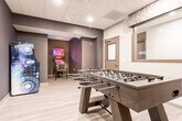 Located at 349 Green St in Woodbridge, NJ, this single-floor game room is a well-appointed recreational space designed for entertainment and social engagement. The layout is divided into two distinct zones that flow seamlessly into one another, creating a cohesive and dynamic environment.

The main area centers around a full-size foosball table positioned on light wood-look flooring, which contrasts attractively with the space's darker design accents. A standout feature of this zone is the textured stacked-wood accent wall, which adds warmth and depth to the room. Mounted directly on this wall is a large flat-screen television, making the area equally suited for watching and gaming. Recessed ceiling lighting and a drop tile ceiling contribute to the clean, modern aesthetic, while a large framed mirror on an adjacent wall enhances the sense of openness.

Tucked into an adjoining alcove, the arcade section offers a more intimate atmosphere. Deep charcoal-toned walls set a dramatic backdrop for a classic multi-game arcade cabinet and a Corvette-themed pinball machine, both fully illuminated and ready for play. A wooden bench provides seating nearby. The transition between the main room and arcade nook is defined by a bold color shift, giving each area its own distinct character while maintaining a unified, contemporary design throughout.