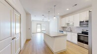 Located at 12020 Brush Hill Rd in Wildwood, Florida, this well-designed single-story home offers three bedrooms, two bathrooms, and three closets within a thoughtfully arranged floor plan. The open-concept kitchen serves as the heart of the home, showcasing crisp white shaker cabinetry, granite countertops, a large center island with pendant lighting, and a full suite of stainless steel appliances including a refrigerator with ice maker, electric range, and built-in microwave. Light hardwood flooring flows throughout the main living areas, complementing the bright, neutral palette and recessed lighting overhead. Ceiling fans are installed in both the kitchen and living room, enhancing comfort throughout. The living room opens toward a glass door that invites natural light into the space. The bedrooms offer plush carpeting and ample room, while the spacious primary bedroom includes a walk-in closet with built-in wire shelving. The primary bathroom features a granite double vanity, white cabinetry, and a glass-enclosed walk-in shower. The second bathroom is equally well-appointed with a granite vanity and a tiled shower-tub combo. Clean white walls and consistent finishes throughout give this home a cohesive, modern feel.