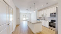 Located at 12020 Brush Hill Rd in Wildwood, Florida, this well-designed single-story home offers three bedrooms, two bathrooms, and three closets within a thoughtfully arranged floor plan. The open-concept kitchen serves as the heart of the home, showcasing crisp white shaker cabinetry, granite countertops, a large center island with pendant lighting, and a full suite of stainless steel appliances including a refrigerator with ice maker, electric range, and built-in microwave. Light hardwood flooring flows throughout the main living areas, complementing the bright, neutral palette and recessed lighting overhead. Ceiling fans are installed in both the kitchen and living room, enhancing comfort throughout. The living room opens toward a glass door that invites natural light into the space. The bedrooms offer plush carpeting and ample room, while the spacious primary bedroom includes a walk-in closet with built-in wire shelving. The primary bathroom features a granite double vanity, white cabinetry, and a glass-enclosed walk-in shower. The second bathroom is equally well-appointed with a granite vanity and a tiled shower-tub combo. Clean white walls and consistent finishes throughout give this home a cohesive, modern feel.