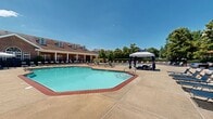 Located at 4048 Mooncoin Way in Lexington, Kentucky, this expansive outdoor amenity space is designed to serve as a premier recreational retreat for residents. The centerpiece of the area is a dual-pool configuration, both finished with classic brick coping and filled with clear, inviting water. One pool features a wide, shallow entry with gently sloping steps, ideal for easy access, while the second offers a spacious open layout surrounded by an extensive concrete sun deck.

The pool deck is outfitted with numerous chaise lounges, including both traditional and modern sling-style chairs, providing ample space for sunbathing. Patio umbrellas offer shaded respite throughout the deck area. A charming gazebo with a cupola-style roof serves as a focal point between the two pools, providing a shaded gathering area with views of the surrounding greenery.

A brick clubhouse building with white columns, dormer windows, and a covered porch overlooks the pool area, lending the space a refined architectural character. A secondary patio area adjacent to the clubhouse features modular outdoor sofas and lounge chairs for relaxed social gatherings. The entire complex is enclosed by black iron fencing, framed by mature trees and manicured landscaping that enhance both privacy and ambiance.