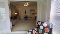 This two-floor residence offers a thoughtfully arranged living environment with a warm and functional layout. The main living area is anchored by plush seating and a glass-top coffee table, creating an inviting space for relaxation and entertainment. A ceiling fan with an integrated light fixture provides both comfort and ambient lighting, while carpet flooring adds a cozy feel underfoot. The open layout allows for a natural flow between the living room and surrounding spaces, enhancing the sense of openness. A glimpse into the kitchen reveals white appliances and cabinetry, reflecting a clean and practical design. Accent lighting from floor lamps adds warmth to the interior, complementing the neutral wall tones throughout. A large mirrored surface near the entryway helps to reflect light and visually expand the space. The home's two-floor configuration provides separation between living and private areas, offering both functionality and comfort. Overall, the space presents a straightforward and livable environment suited for everyday residential use.