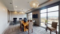Located at 4015 Aspen Grove Drive in Franklin, Tennessee, this single-floor business center offers a polished, contemporary environment designed for both collaboration and focused work. The space is defined by its open, well-proportioned layout, featuring patterned carpet tile flooring in cool grey tones that lends a professional yet welcoming feel throughout.

At the heart of the room sits a solid wood conference table surrounded by upholstered chairs, ideal for meetings or group gatherings. Elegant pendant light fixtures — including a distinctive capiz shell globe chandelier — add a refined decorative touch to the tray ceiling above. A wall-mounted flat-screen television serves the meeting area, enhancing its functionality for presentations.

A dedicated workstation zone lines one wall, equipped with multiple desktop computers on sleek white benching, ergonomic task chairs, and a printer, catering to productivity needs. Textured accent walls in warm silver tones contribute depth and sophistication to the interior.

Floor-to-ceiling windows along two walls flood the space with abundant natural light while framing sweeping views of the surrounding Franklin skyline and rolling Tennessee hills. Sliding glass doors open directly onto an outdoor terrace furnished with seating, extending the usable space and offering a refreshing open-air retreat with panoramic views.