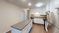 Located at 2601 S Kiwanis Ave in Sioux Falls, South Dakota, this single-floor unit offers a well-designed, open layout with a comfortable and functional flow throughout. The living area is bright and generously sized, featuring rich dark hardwood-style flooring, neutral warm-toned walls, a textured ceiling, and a wall-mounted air conditioning unit alongside baseboard heating. A sliding glass door floods the space with natural light and provides access to an outdoor area.

The kitchen is a standout feature, outfitted with crisp white cabinetry, granite-style countertops, and a full suite of stainless steel appliances including a range, microwave, and refrigerator. A center island with additional counter space adds practicality, while a separate built-in buffet area with glass-front upper cabinets provides ample storage and display potential. The hardwood-style flooring continues seamlessly throughout the kitchen and main living areas.

The bedrooms are carpeted for comfort, with windows offering natural light and views of the surrounding neighborhood. Two full bathrooms each include a tub-shower combination, white vanity cabinetry, and granite-style countertops. A dedicated in-unit laundry area accommodates a full-size washer and dryer with overhead cabinetry above for extra storage.