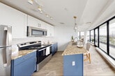 Located at 50-54 Sussex Avenue in Newark, NJ, this thoughtfully designed studio offers a seamless open-plan layout combining the kitchen and living area into one cohesive space. The kitchen is a standout feature, showcasing a two-tone design with crisp white upper cabinetry and navy blue lower cabinets, all complemented by granite countertops. A central island with seating provides additional prep space and a casual dining option, while stainless steel appliances and pendant lighting with gold accents add a polished, modern finish. Track lighting overhead further enhances functionality.

The living area transitions naturally from the kitchen, anchored by a dramatic curved wall of floor-to-ceiling black-framed windows that flood the space with natural light and frame sweeping panoramic views of the Newark skyline and surrounding cityscape. Light wood-look tile flooring runs throughout, contributing to the bright, airy atmosphere. A sliding glass door opens onto a private balcony, extending the living space outdoors. A stacked in-unit washer and dryer is conveniently tucked near the entryway. The bathroom features large-format dark slate tile flooring and clean white walls, offering a calm, minimalist aesthetic. This elevated residence combines contemporary design with exceptional urban views.