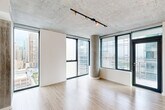 Located on the 18th floor of a modern high-rise in Chicago's South Loop neighborhood, this 2-bedroom, 2-bathroom residence offers a compelling blend of industrial design and contemporary finishes. The open-concept living and kitchen area is anchored by floor-to-ceiling windows that frame sweeping views of the Chicago skyline, allowing abundant natural light to fill the space. Exposed concrete ceilings and a distinctive cylindrical concrete column lend an industrial character, while light wood-tone flooring throughout creates a warm contrast.

The kitchen is well-appointed with dark wood cabinetry, stainless steel appliances including a gas range, microwave, and refrigerator, a mosaic tile backsplash, and a spacious white countertop island with an undermount sink. Both bedrooms feature large windows with city views and the same warm wood flooring under exposed concrete ceilings. The primary bedroom is generously sized with a dedicated closet. The two bathrooms are finished with neutral tile, including a glass-enclosed walk-in shower. Additional conveniences include an in-unit laundry area equipped with a washer and dryer, and a hallway connecting the private spaces of the home.