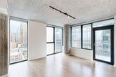 Located on the 18th floor of a modern high-rise in Chicago's South Loop neighborhood, this 2-bedroom, 2-bathroom residence offers a compelling blend of industrial design and contemporary finishes. The open-concept living and kitchen area is anchored by floor-to-ceiling windows that frame sweeping views of the Chicago skyline, allowing abundant natural light to fill the space. Exposed concrete ceilings and a distinctive cylindrical concrete column lend an industrial character, while light wood-tone flooring throughout creates a warm contrast.

The kitchen is well-appointed with dark wood cabinetry, stainless steel appliances including a gas range, microwave, and refrigerator, a mosaic tile backsplash, and a spacious white countertop island with an undermount sink. Both bedrooms feature large windows with city views and the same warm wood flooring under exposed concrete ceilings. The primary bedroom is generously sized with a dedicated closet. The two bathrooms are finished with neutral tile, including a glass-enclosed walk-in shower. Additional conveniences include an in-unit laundry area equipped with a washer and dryer, and a hallway connecting the private spaces of the home.