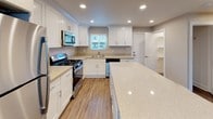 This single-floor 1-bedroom, 1-bathroom residence offers a thoughtfully designed layout that maximizes comfort and functionality. The kitchen is a standout feature, showcasing crisp white shaker cabinetry, light quartz countertops, and a central island that provides additional prep space and seating. A full suite of stainless steel appliances — including a gas range, built-in microwave, dishwasher, and refrigerator — completes the modern aesthetic. Recessed lighting and a window above the sink bring in natural light, enhancing the clean, bright atmosphere. The open-concept living area flows seamlessly from the kitchen and is finished with warm wood-style luxury vinyl plank flooring and a ceiling fan with integrated light fixture. Large windows invite natural light and outdoor views into the space. The bedroom is carpeted for added comfort, features a ceiling fan, and includes a sliding glass door with vertical blinds that opens to an outdoor area. The full bathroom is well-appointed with a tub/shower combo, a white vanity with stone-topped counters, and a large mirror. A built-in shelving nook adds convenient storage. The consistent neutral color palette and cohesive finishes throughout create a calm, move-in-ready environment.