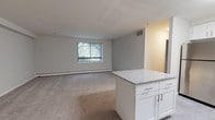 Located at 300 E Marshall St in West Chester, PA, this single-floor unit offers a clean, functional layout designed for comfortable everyday living. The open-concept living and dining area is finished with plush carpeting and neutral gray walls, creating a bright and inviting atmosphere. A large window fitted with vertical blinds allows natural light to fill the space while offering views of the surrounding greenery.

The kitchen is a standout feature, boasting white shaker-style cabinetry, granite-look countertops, and a full suite of stainless steel appliances including a range, over-the-range microwave, dishwasher, and refrigerator. A central island provides additional counter space and serves as a natural divider between the kitchen and living area.

The bedroom is generously sized with soft carpeting, baseboard heating, and a window that brings in natural light and outdoor views, making it a peaceful retreat. The full bathroom features classic white tile surrounding a soaking tub and shower combination, with tile flooring for easy maintenance.

The entryway provides a practical transition into the unit, with the electrical panel conveniently accessible nearby. Throughout the space, the neutral color palette, modern finishes, and well-proportioned rooms come together to create a cohesive and move-in-ready living environment.