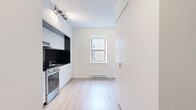 Located on Rue Sherbrooke Ouest in Montréal, this studio presents a thoughtfully designed open-concept layout that maximizes every square foot. Light-toned laminate flooring runs throughout the main living area, complementing the crisp white walls and creating a bright, airy atmosphere. Multiple windows allow natural light to flow in, offering views of the surrounding urban streetscape.

The kitchen is a standout feature, outfitted with sleek white cabinetry extending to the ceiling, a bold black square-tile backsplash, dark countertops, and stainless steel appliances including a full range and refrigerator. A built-in range hood and under-cabinet lighting add to the kitchen's polished, functional character.

A full-height white partition wall divides the living and sleeping areas, incorporating integrated storage and housing a wall-mounted mini-split air conditioning unit. The entryway is anchored by a dark, solid door with a modern handle, adding a contemporary contrast to the otherwise light interior.

The bathroom is finished with floor-to-ceiling white square tiles, a frameless sliding glass shower enclosure, and coordinating mosaic tile flooring, delivering a clean and modern aesthetic. Baseboard heating runs along the perimeter of the living space, ensuring year-round comfort. This studio offers a well-appointed, efficient urban retreat in a prime Montréal location.