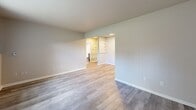 Located at 2345 Harrison Ave in East Lansing, Michigan, this one-bedroom unit offers a efficiently designed single-floor layout. The interior is finished with light wood-style luxury vinyl flooring throughout, neutral gray walls, and clean white trim, creating a bright and cohesive aesthetic.

The kitchen is a standout feature, outfitted with dark wood-grain cabinetry spanning both upper and lower sections, a sleek white countertop, and a stainless steel sink. Stainless steel appliances, including a refrigerator, microwave, and electric range, complete the space. Recessed lighting adds a modern touch and ensures the area is well-lit.

The living area is open and clean, with smooth walls and consistent flooring that carries throughout the unit. A doorway connects the main living space to the bedroom wing, which also includes built-in shelving visible through the hallway.

The bedroom is a comfortable size, featuring a window with vertical blinds that allows natural light to filter in. A set of louvered bi-fold closet doors provides ample storage. A baseboard heating unit runs along the lower wall, ensuring year-round comfort.

The unit's straightforward, modern design and functional layout make it a practical and attractive living space in the East Lansing area.