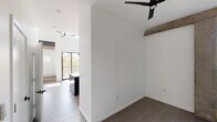 This contemporary two-story space showcases a bold, modern aesthetic defined by a striking monochromatic palette and thoughtful architectural details. The open-concept lower level features large-format tile flooring and soaring double-height ceilings, with exposed concrete beams adding an industrial character that complements the clean white walls. Floor-to-ceiling sliding glass doors flood the living area with natural light and provide views of the surrounding greenery, while ceiling fans with matte black finishes contribute to the cohesive design language throughout.

The kitchen is a dramatic focal point, outfitted with floor-to-ceiling matte black cabinetry, dark granite countertops, black tile backsplash, and a full suite of black appliances. Pendant lighting and a dedicated sink island enhance both functionality and visual impact.

The upper floor is accessed via an open staircase with sleek black metal and glass railings, offering a bird's-eye view of the levels below. Tall vertical windows and a centered horizontal window bathe the upper level in natural light, creating a bright, airy atmosphere.

The bathroom continues the modern theme with white subway tile, a glass-enclosed walk-in shower, matte black fixtures and hardware, and a white vanity with an undermount sink — delivering a clean, spa-like finish throughout.