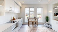 Located at 308 Puyallup Ave in Tacoma, WA, this efficiently designed studio unit offers a bright, open-concept living space spread across a single floor. The interior is characterized by crisp white walls, wood-look plank flooring, and abundant natural light throughout.

The kitchen is a standout feature, outfitted with two-tone cabinetry — white upper cabinets and soft gray lower cabinets — paired with clean white countertops and modern brushed nickel hardware. It includes a flat-top cooktop, under-counter microwave, stainless steel sink, and refrigerator, along with open display shelving for added functionality and style. Large windows adjacent to the kitchen flood the living and dining area with natural light while offering elevated views of the surrounding Tacoma cityscape.

The hallway entrance provides a welcoming transition into the unit, with recessed lighting and a ceiling fan enhancing comfort in the main living area. The bathroom is clean and functional, featuring wood-look flooring, a shower/tub combination with a curtain rod, and simple, neutral finishes consistent with the rest of the unit.

Overall, the space maintains a modern, minimalist aesthetic with a light and airy ambiance, making efficient use of every square foot.