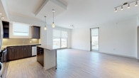 This contemporary single-floor residence offers a thoughtfully designed open-concept layout that seamlessly connects the kitchen, dining, and living areas. Light wood-tone flooring runs throughout, complementing the clean white walls and creating a bright, cohesive aesthetic.

The kitchen is a standout feature, equipped with rich dark wood cabinetry, granite countertops, a tile backsplash, and a full suite of stainless steel appliances, including a range, microwave, and dishwasher. A peninsula with pendant lighting provides additional counter space and serves as a casual dining or gathering point. Large windows and a glass door in the living area flood the open space with natural light and offer views of the surrounding neighborhood.

The bedrooms are generously sized with the same wood-tone flooring and roller shade windows that allow for flexible light control. The primary suite includes access to a spacious walk-in closet with built-in shelving and hanging rods, providing ample storage. Both bathrooms feature striking marble-style tile flooring and wall surrounds. The primary bathroom includes a glass-enclosed walk-in shower with a bench, a dual-sink vanity with dark cabinetry, and a large illuminated mirror. The secondary bathroom also features a glass-enclosed shower with marble tile detailing.